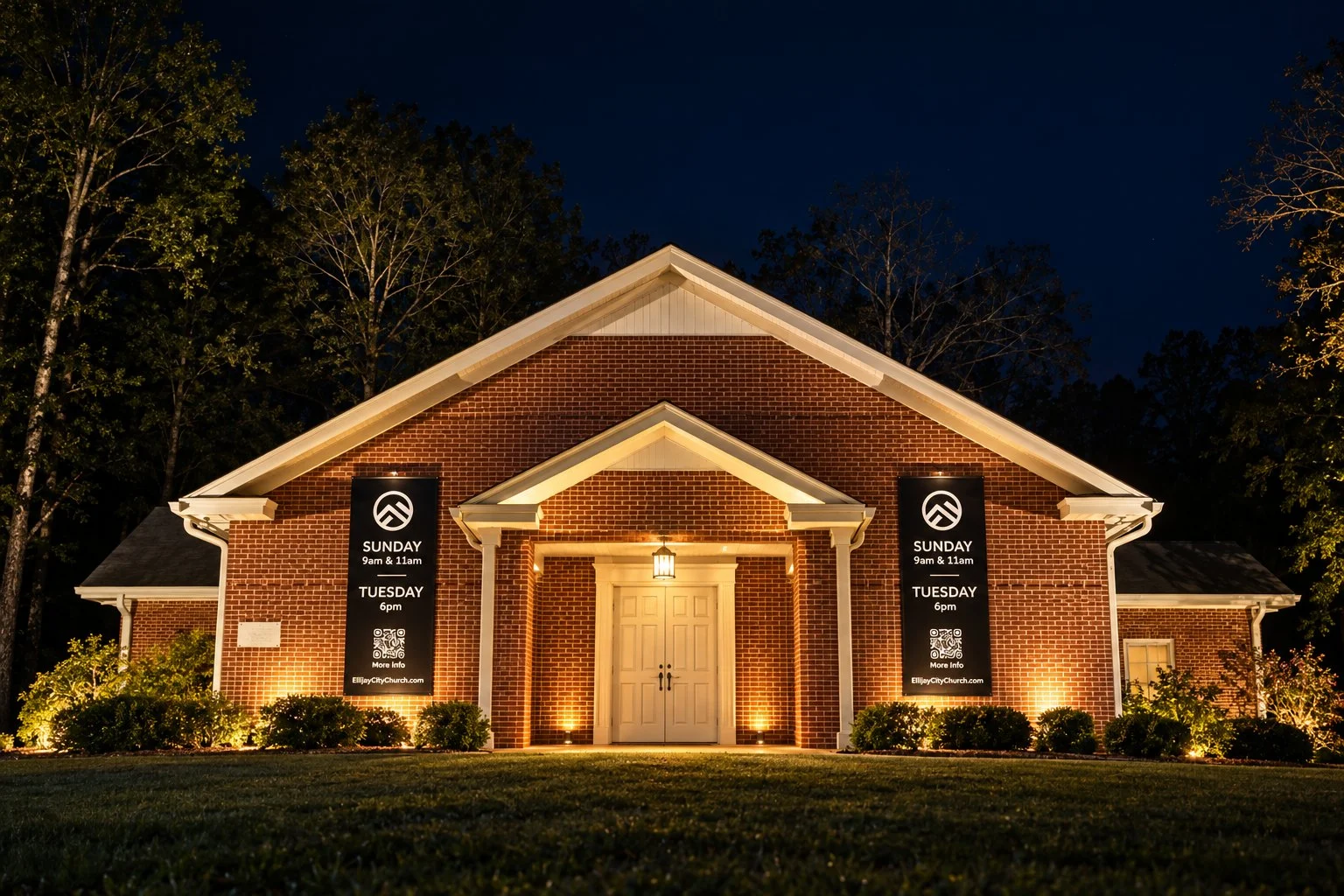 Ellijay City Church at night: the red brick building lit warmly, with white double doors and black service-time banners on each side of the porch